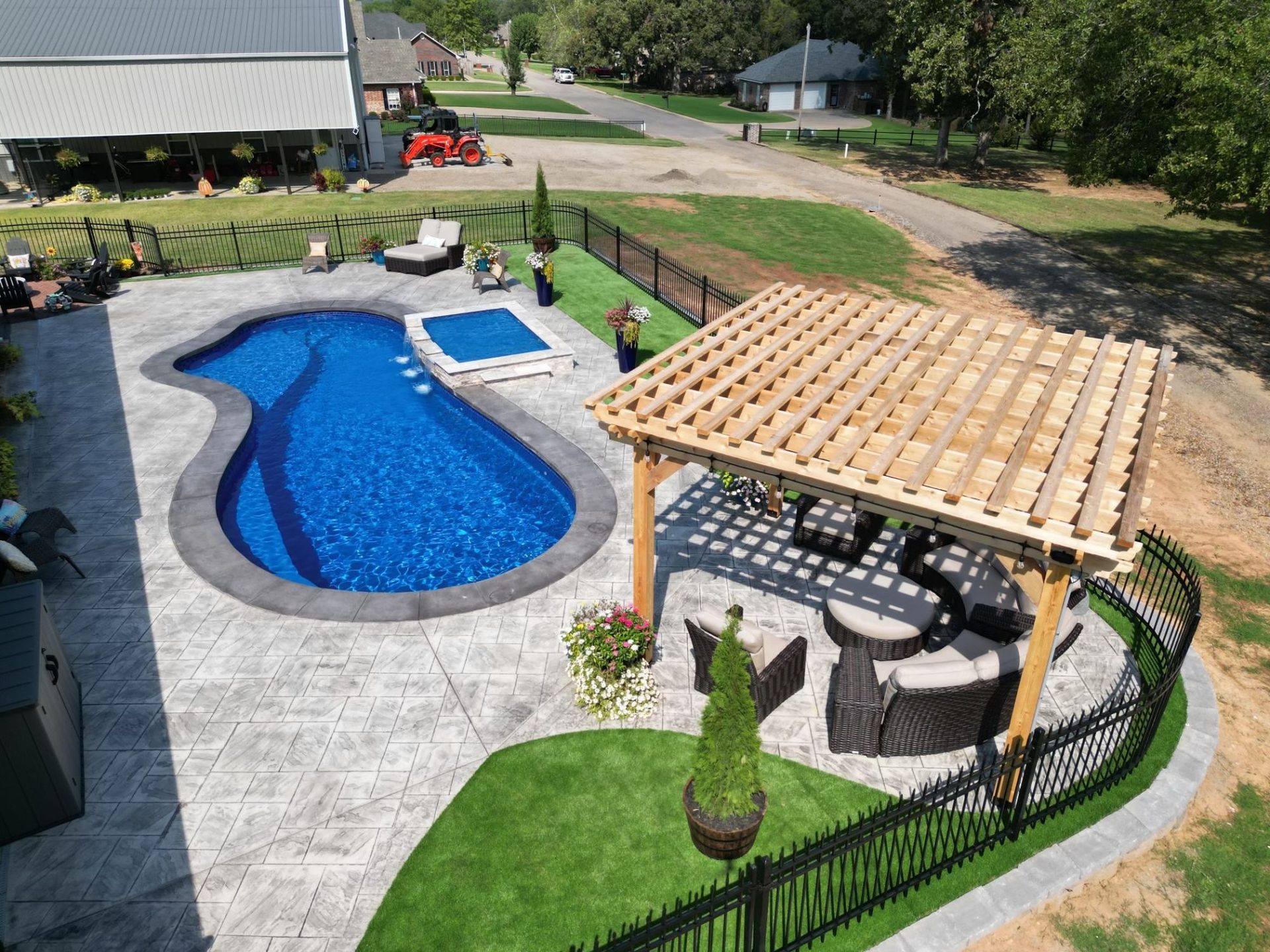 Freeform fiberglass pool with spillover spa and pergola in a finished backyard